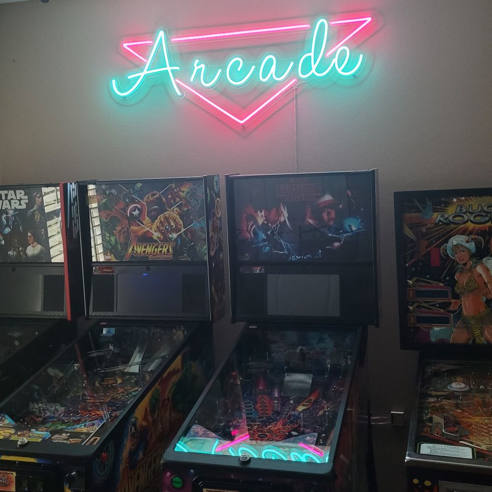 Custom Neon® LED arcade sign in pink and ice blue shown above retro pinball machines