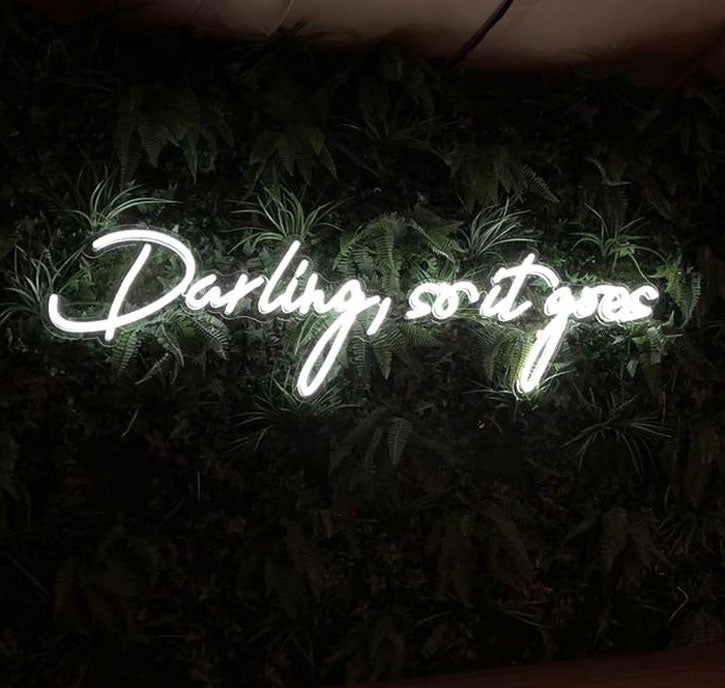 Darling, so it goes Neon Sign Quote for Weddings & Home Decor shown on green wall
- photo from CustomNeon.com