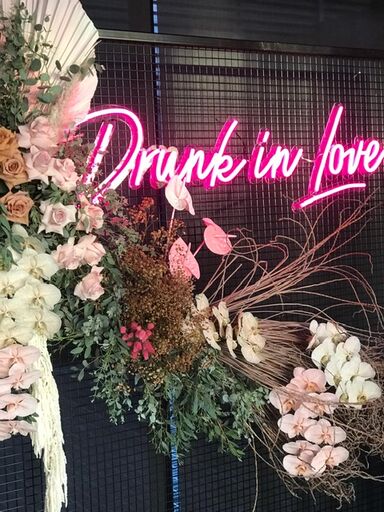 Large LED neon sign Drunk in Love attached to a mesh frame surrounded by floral decorations at an event - photo CustomNeon.com