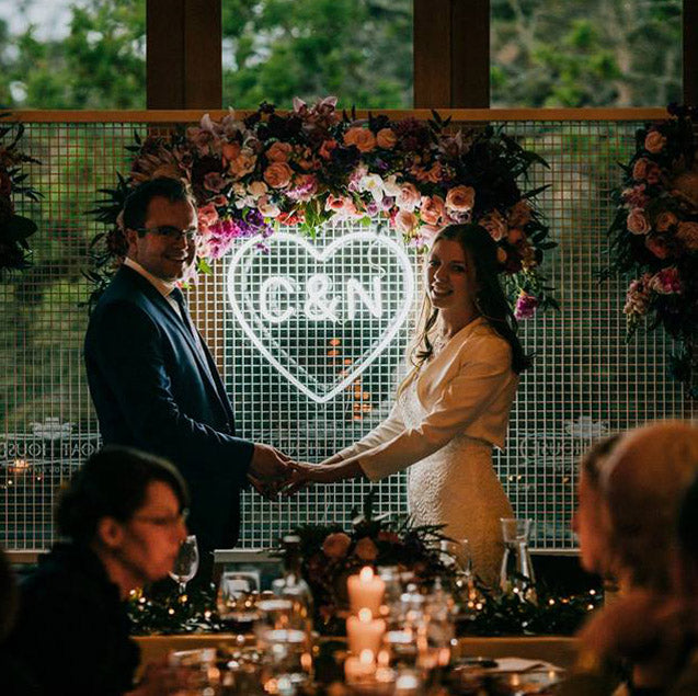 Beautiful LED neon heart light personalized with the bride & groom's initials. Shown here on a mesh background with the happy couple. Photo from CustomNeon.com