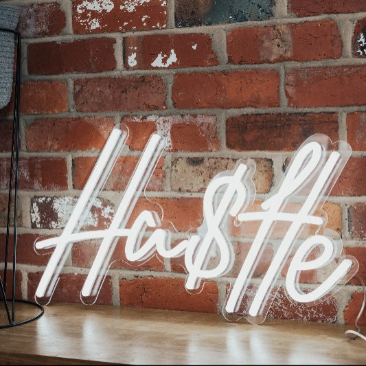 Hustle Neon Sign shown on an exposed brick wall - photo from CustomNeon.com
