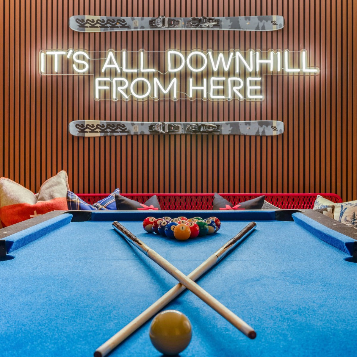It's All Downhill From Here white LED neon sign mounted on wood panel wall between camo colored skis above the pool table in a ski chalet games room - CUSTOM NEON™ x SOMERLED COLLECTION