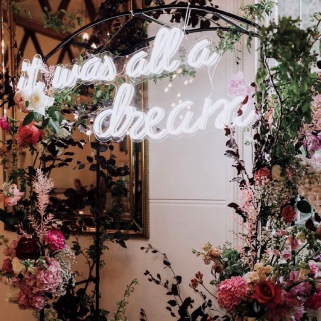 White LED neon quote sign "It was all a dream" attached to a wedding arch with floral arrangements - from Custom Neon
