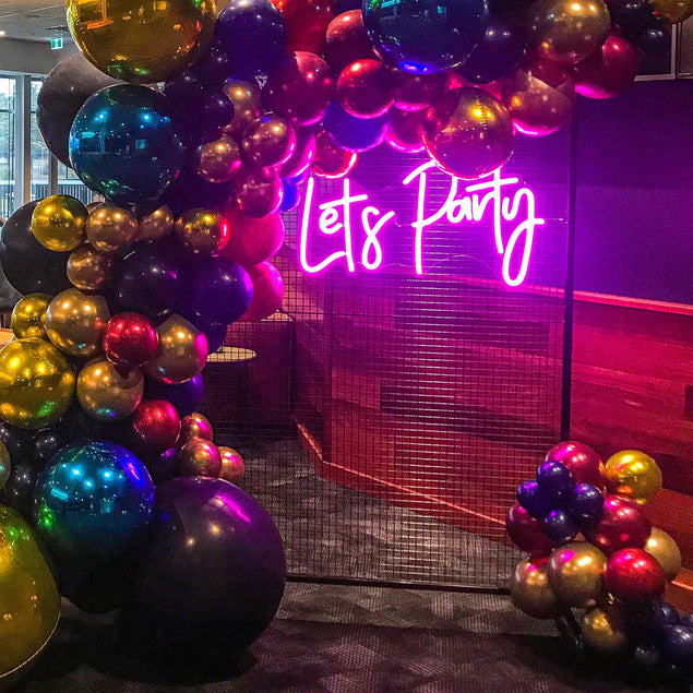 Let's Party portable LED neon sign shown on a wire mesh background surrounded by balloons - photo from CustomNeon.com