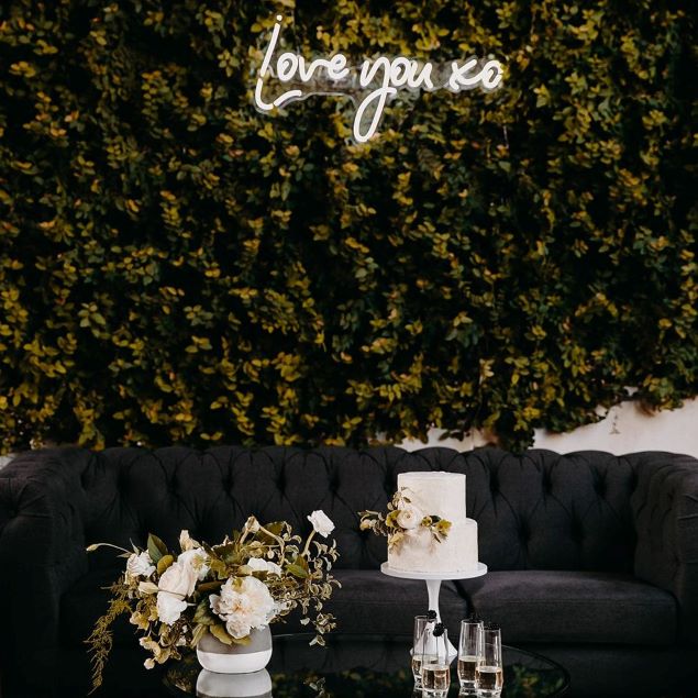 Love You XO LED neon sign on green wall while happy couple hold hands - sign by CustomNeon.com / photo by candileonardphotography.com