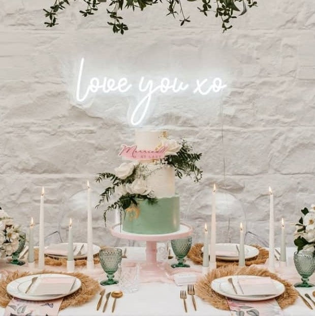 Love You XO LED neon sign on a green photo wall with a floral arrangement and cake in the foreground - sign by CustomNeon.com / photo by candileonardphotography.com