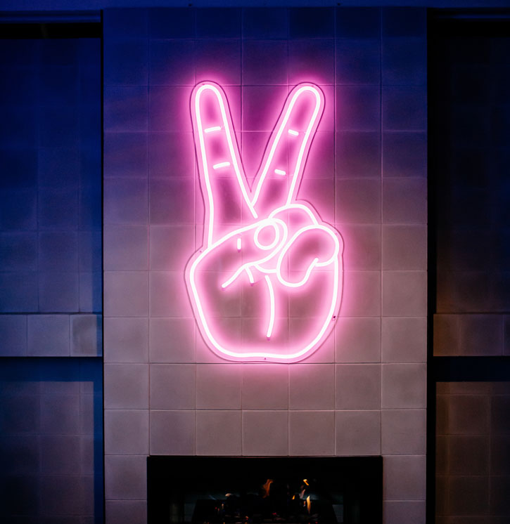 LED Neon Peace Sign shown mounted as wall art above a fireplace - photo from CustomNeon.com