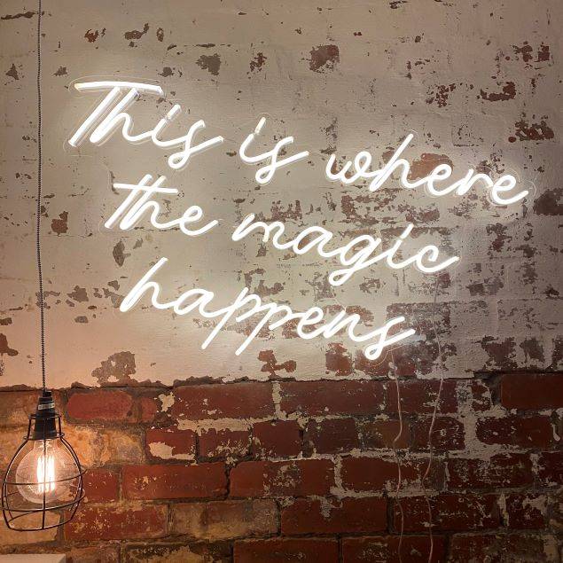 This is Where the Magic Happens white neon flex sign on distressed brick wall @customneon