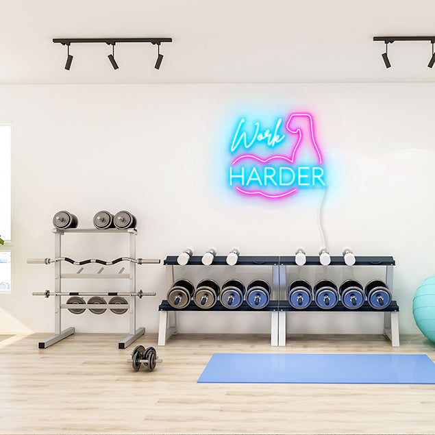 Work Harder pink & blue neon wall art shown on a white gym wall above weights - CUSTOM NEON®