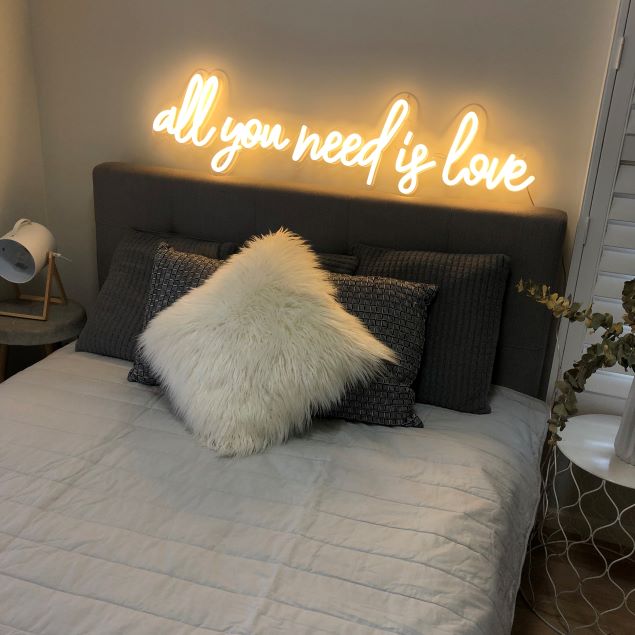 All You Need is Love LED Neon Sign shown above a bed - photo from Custom Neon®