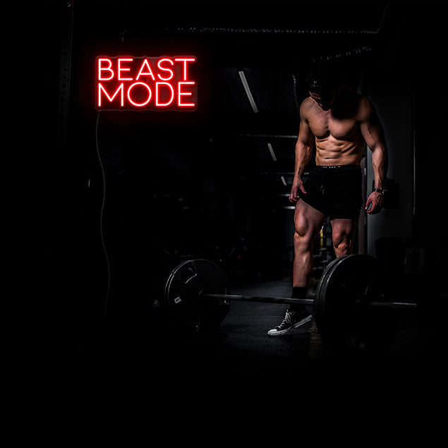 Beast Mode red neon sign shown on black wall behind a man lifting weights - sign by CUSTOM NEON