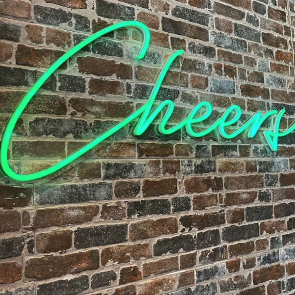 Cheers Neon Bar Sign in green on a brick wall @margaritascantina made by Custom Neon®