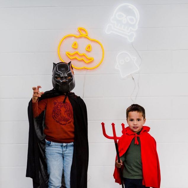 Cute LED neon ghost shown on a white brick wall with Halloween lights above kids in costumes - by Custom Neon®