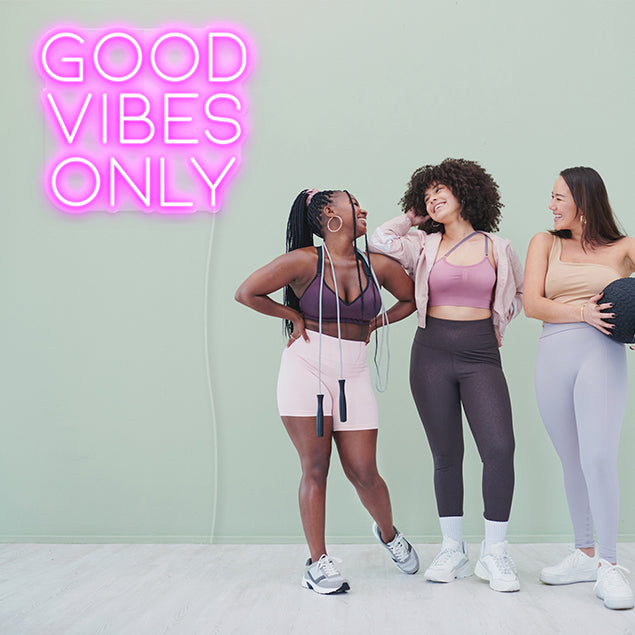 Good Vibes Only pink light up sign shown on moss colored wall