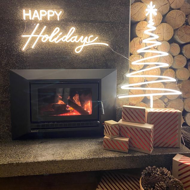 White light up Xmas tree surrounded by a modern wood fireplace