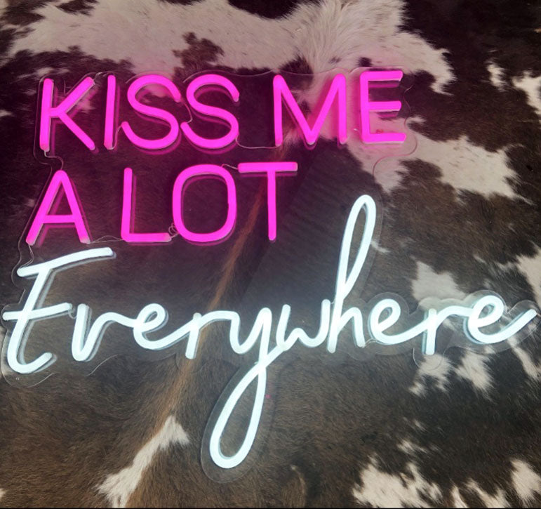 Kiss Me A Lot Everywhere LED Neon Sign in pink and white shown on faux cow hide - photo CustomNeon.com