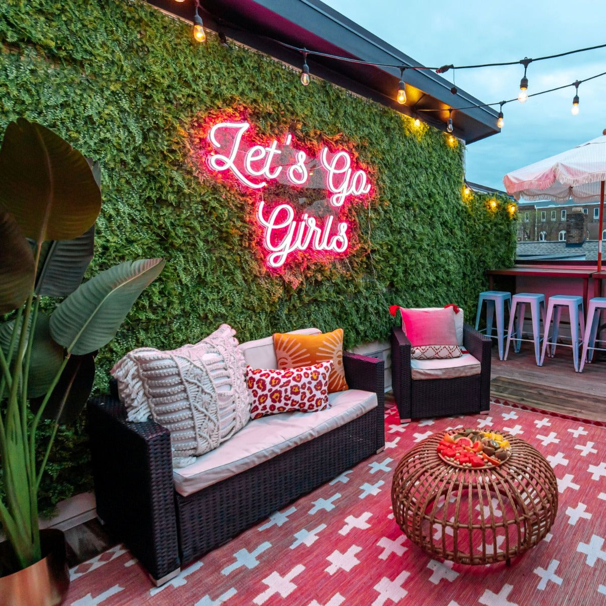 Let's Go Girls pink LED neon sign on a lush greenery wall in an alfresco seating area - CUSTOM NEON™ x SOMERLED COLLECTION