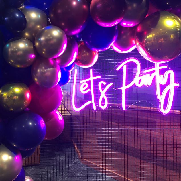 Let's Party portable LED neon sign shown on a wire mesh background surrounded by balloons - photo from CustomNeon.com