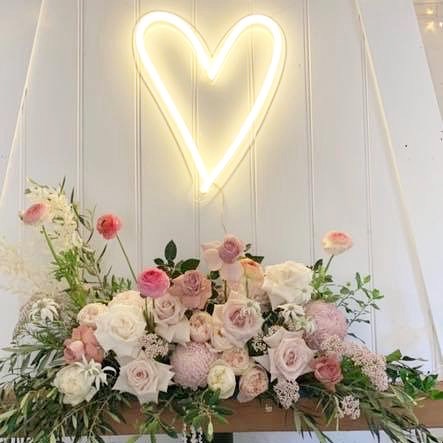 Love heart neon light in warm white wall mounted below floral decorations - Custom Neon