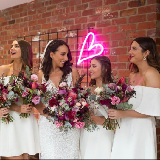 LED neon heart light for wedding decor shown wall mounted in pink with CustomNeon's founder and her bridesmaids - photo from CustomNeon.com