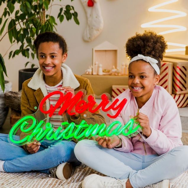 Merry Christmas Red & Green LED Neon Sign by CUSTOM NEON® held by smiling girls with a Nativity scene