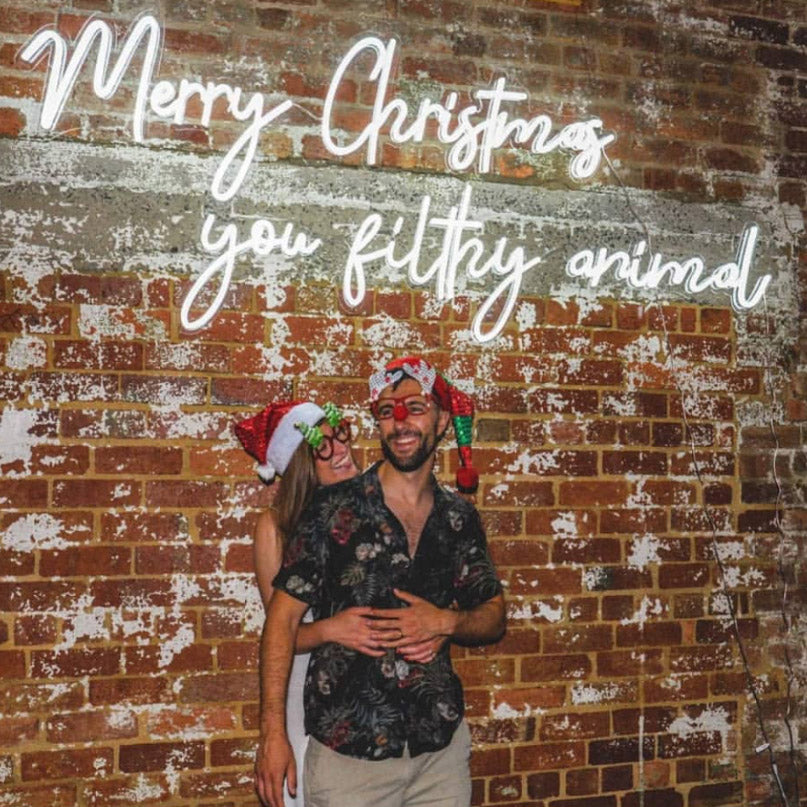 Merry Christmas You Filthy Animal LED Neon Sign shown on an exposed brick wall at a Xmas party - photo from CustomNeon.com