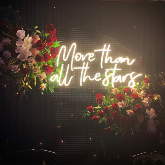 More than all the stars faux neon sign on a mesh screen amidst floral arrangements - from Custom Neon®