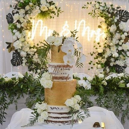 Mr & Mrs light sign in white on a floral arch behind the top table - from Custom Neon