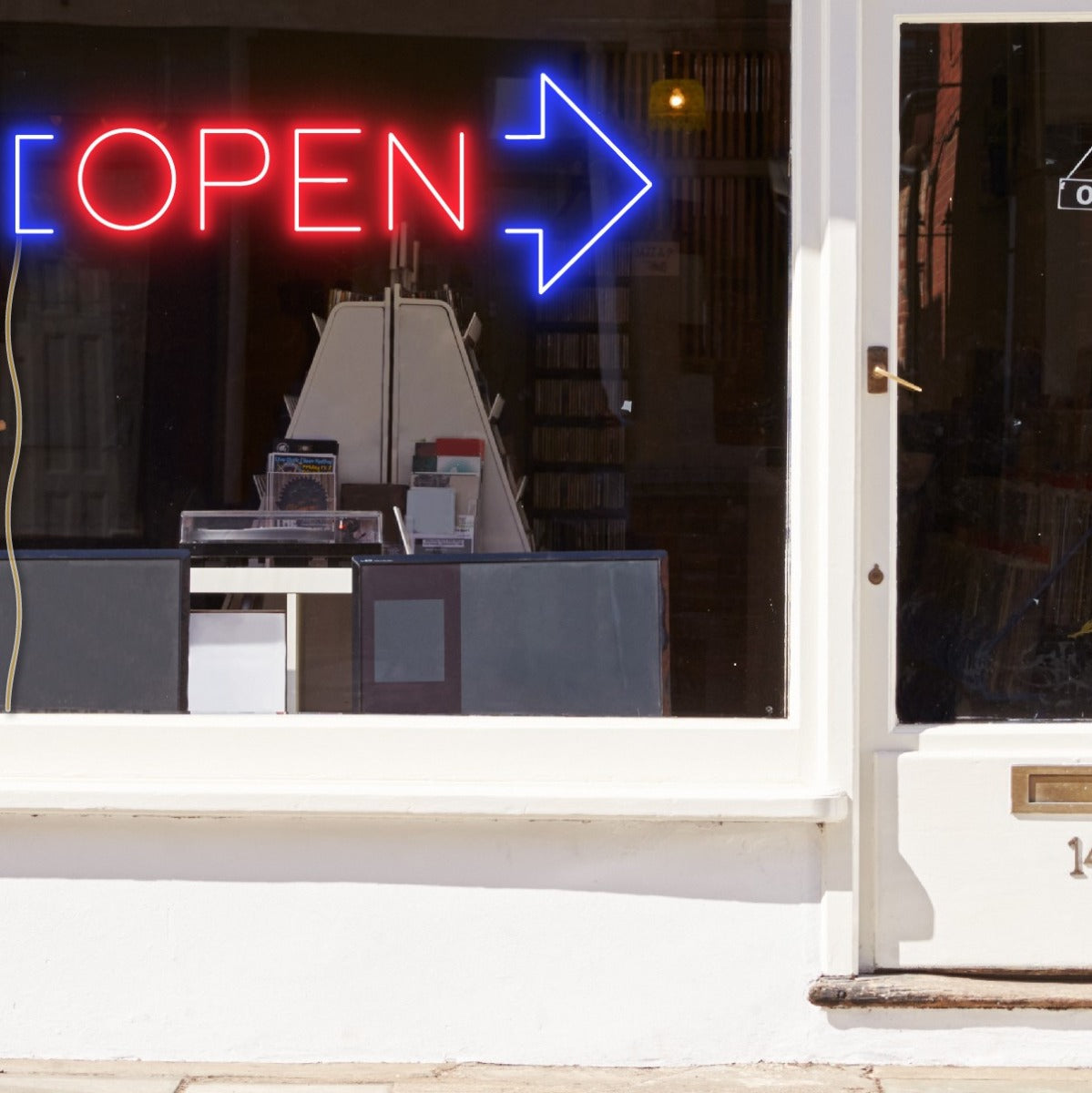 Neon light open sign in red with an oversized blue arrow shown in a shop window - from CustomNeon.com