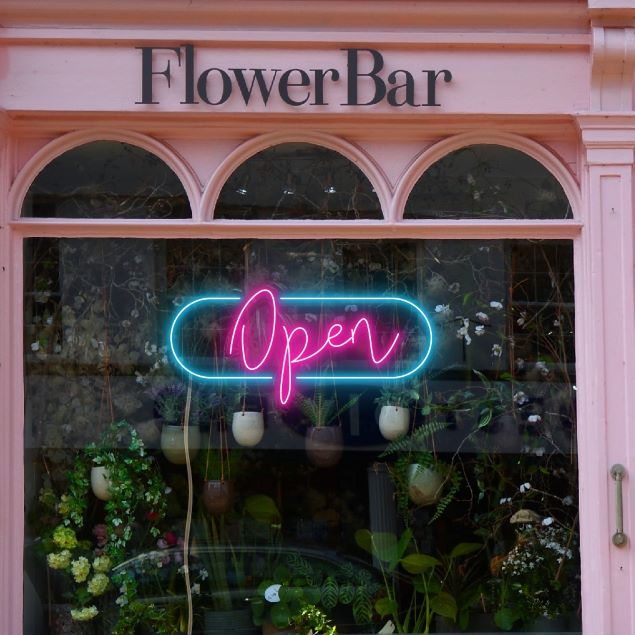 LED Neon Flex open sign in a modern cursive font surrounded by an oblong frame shown in a florist's shop window - from CustomNeon.com