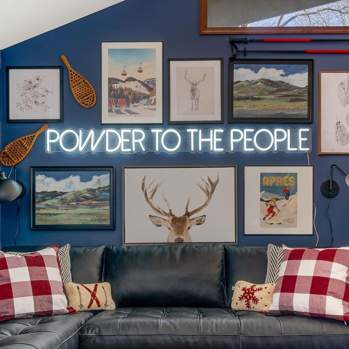 Powder to the People white LED neon sign on a blue feature wall surrounded by framed paintings and prints of mountain scenes and ski slopes - CUSTOM NEON™ x SOMERLED COLLECTION