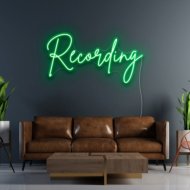 CUSTOM NEON® Recording Sign in green script font on dark grey wall above brown couch