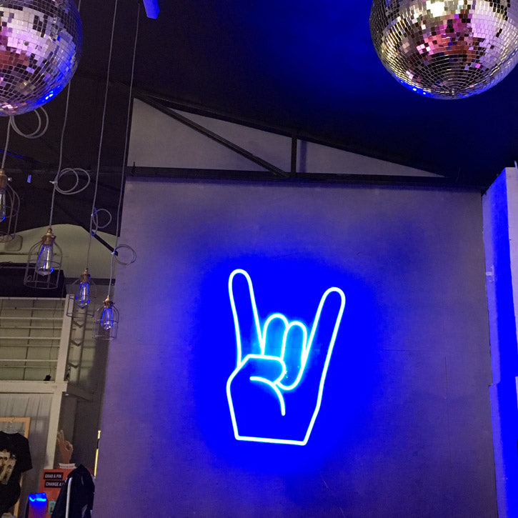 Rock On Emoji LED Neon Sign shown in blue, wall mounted in a fashion store - photo from CustomNeon.com