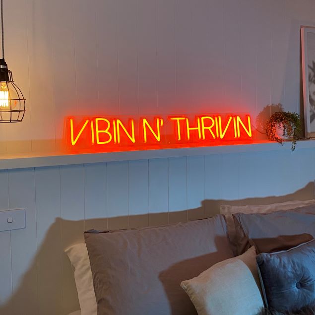 Vibin 'n Thrivin orange neon flex sign shown above a bed from Custom Neon