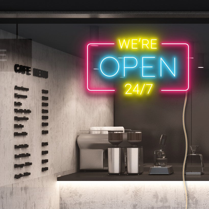 WE'RE OPEN 24/7 neon sign in yellow, blue & pink shown in a cafe window - from CustomNeon.com