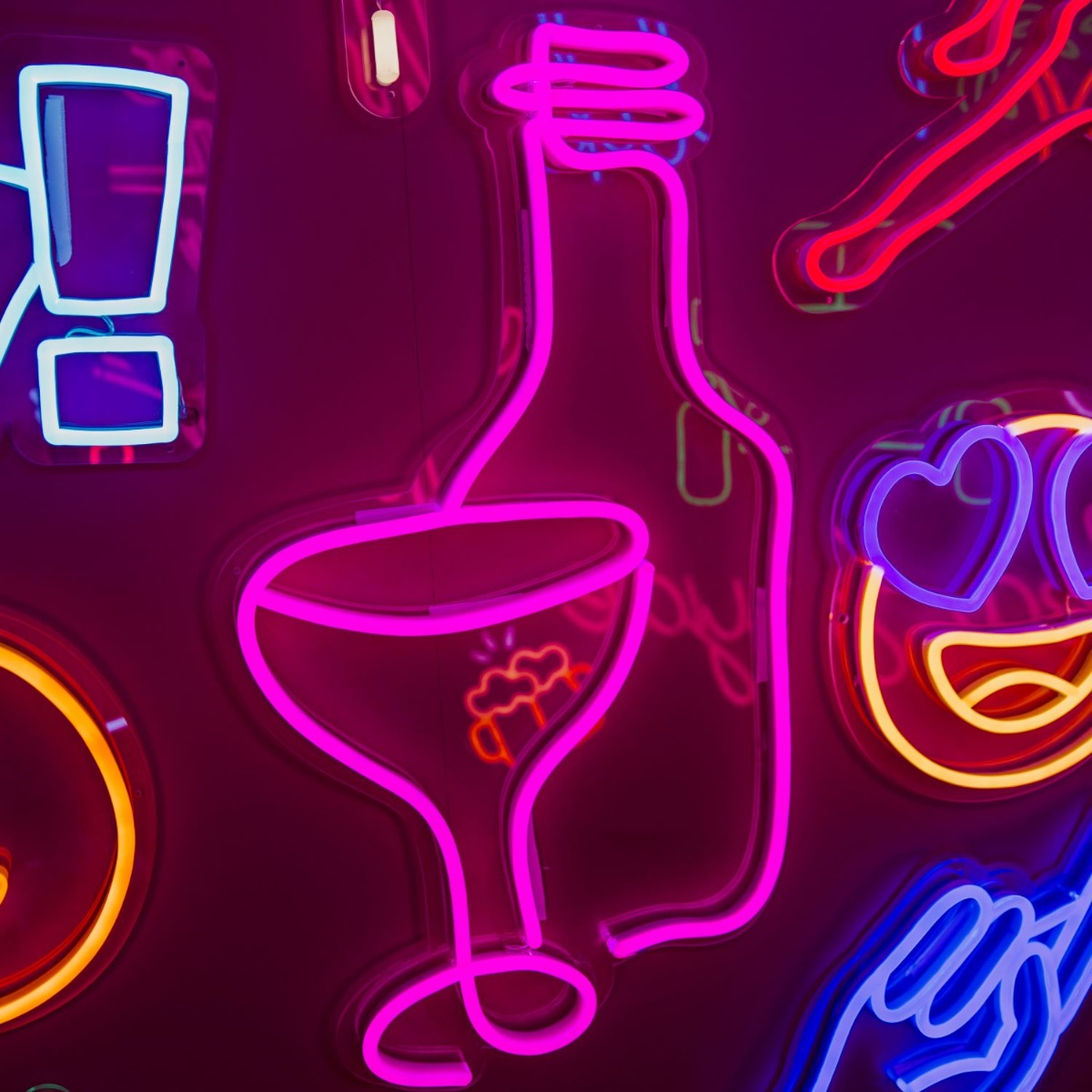 Custom Neon® Wine Glass & Bottle Line Art shown in pink illuminated against a dark pink wall in dim light