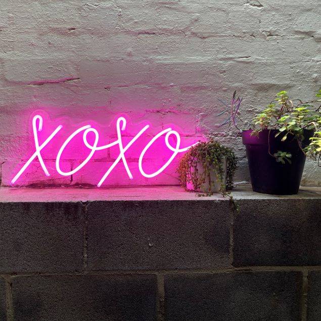 XOXO LED neon sign in pink from Custom Neon® shown against a white brick wall