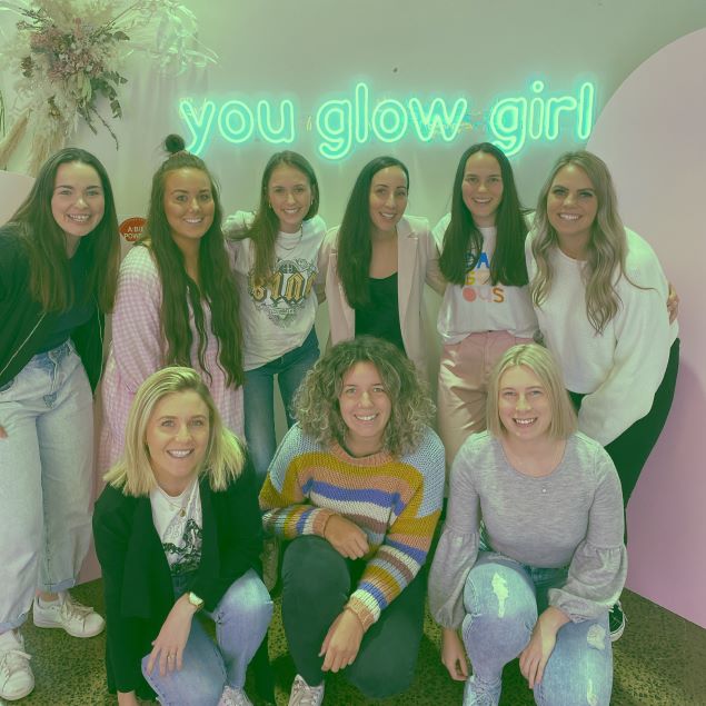 You Glow Girl CUSTOM NEON® sign in mint green behind some of the CUSTOM NEON® team